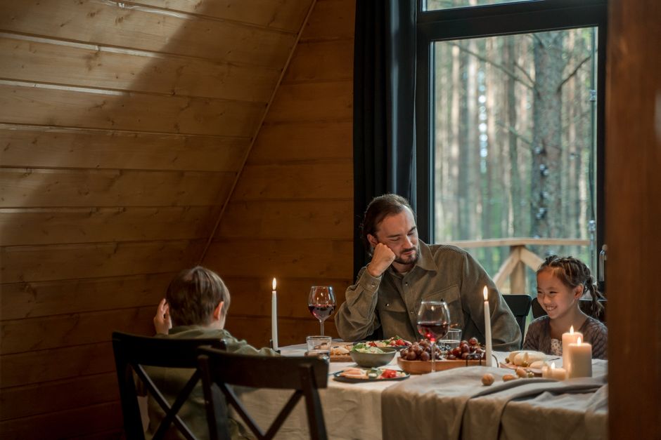 Father enjoying quality time with son and daughter over a candlelit dinner in a wooden cabin.