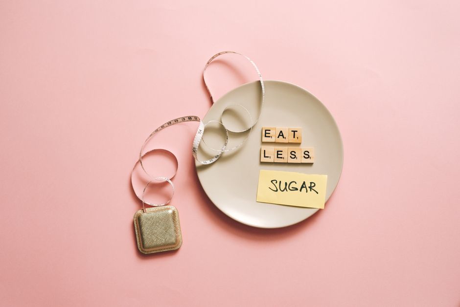 Flat lay of a plate with scrabble tiles spelling 'Eat Less Sugar,' accompanied by a tape measure, symbolizing healthy eating.