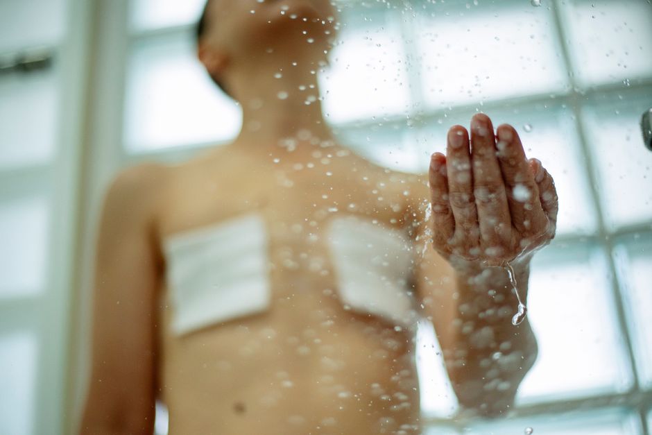 From below of crop unrecognizable shirtless woman with sterile bandages on breast taking shower in bathroom