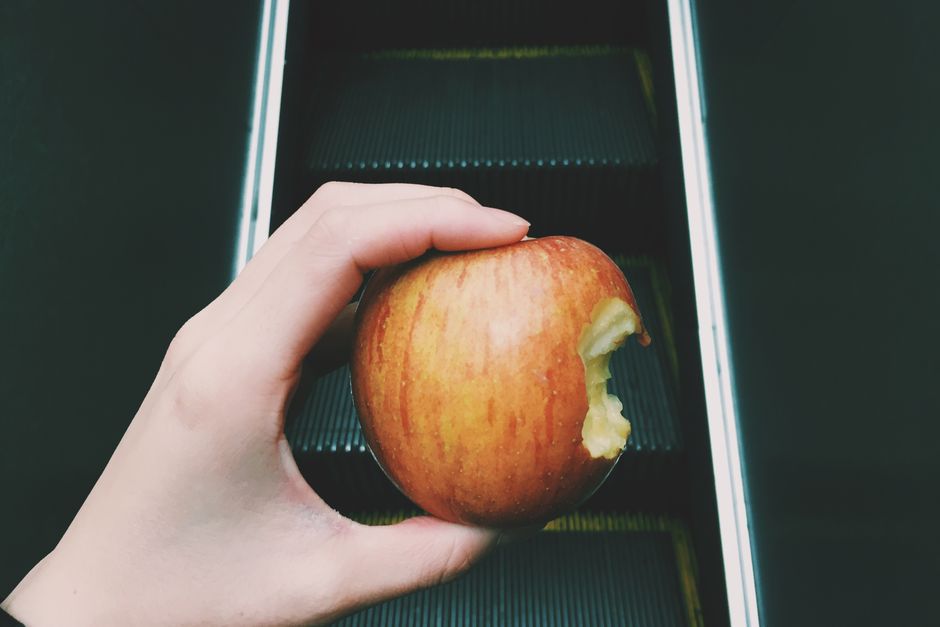 Hand holding a bitten apple on an escalator, showcasing a blend of food and travel concept.
