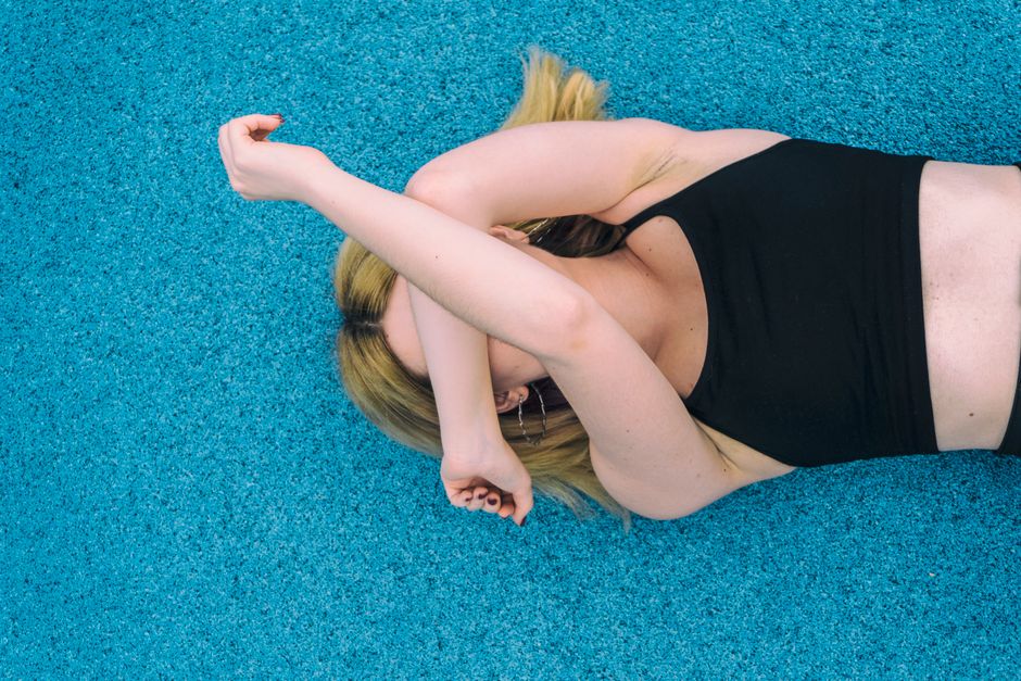 Image of a young woman with blonde hair stretching on a vibrant blue surface.