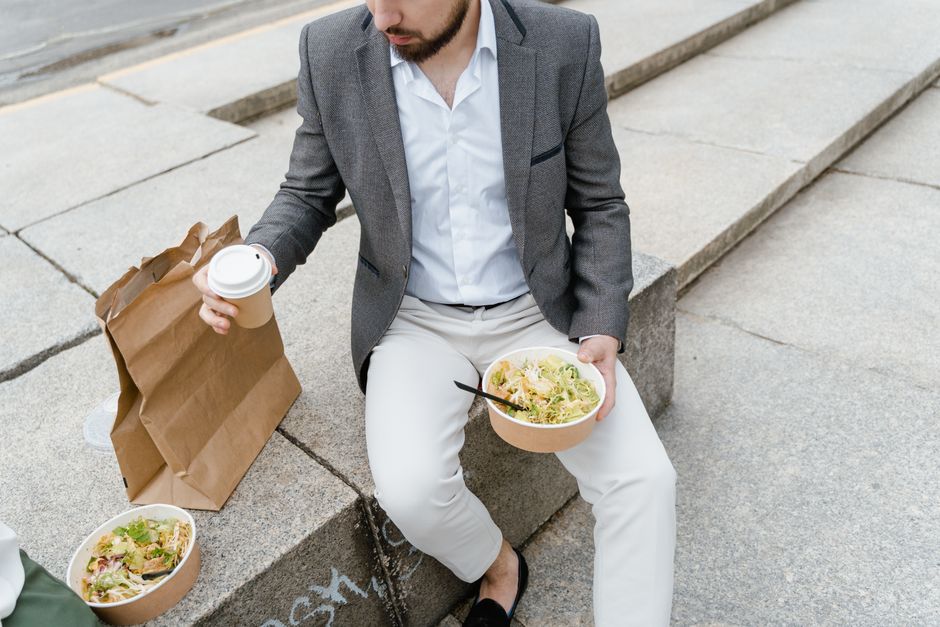 Man in a suit enjoying a takeaway salad and coffee outdoors on city steps.