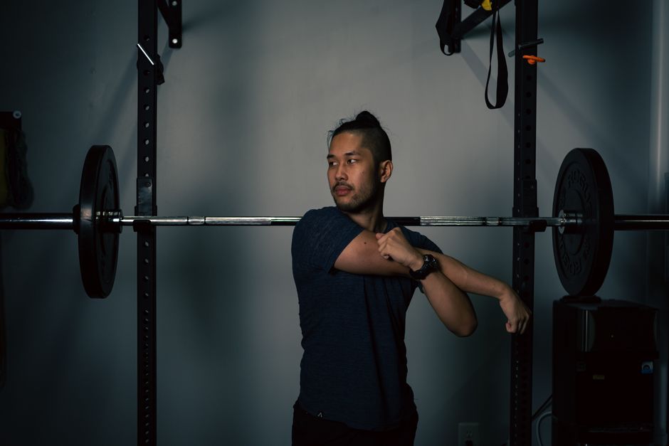 Man stretching near barbell equipment in a home gym, preparing for workout.