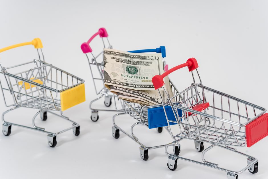 Miniature shopping carts containing dollar bills on a white background.