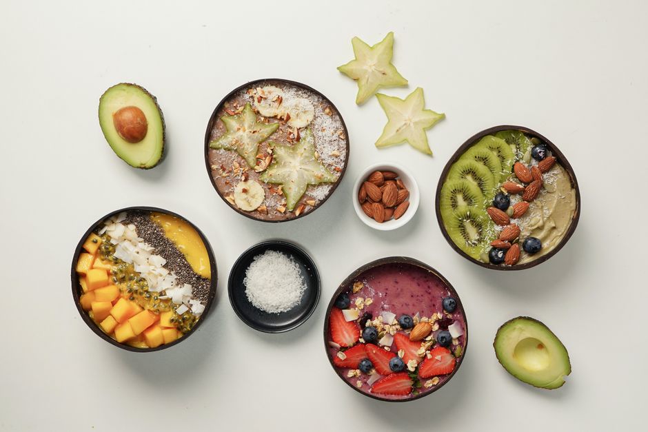 Overhead view of vibrant smoothie bowls with star fruit, kiwi, mango, and avocado on a light background.