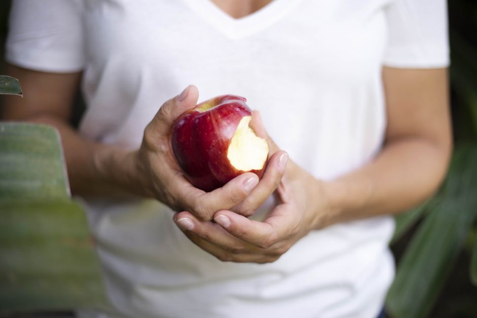 Person holding a bitten red apple, emphasizing healthy eating.