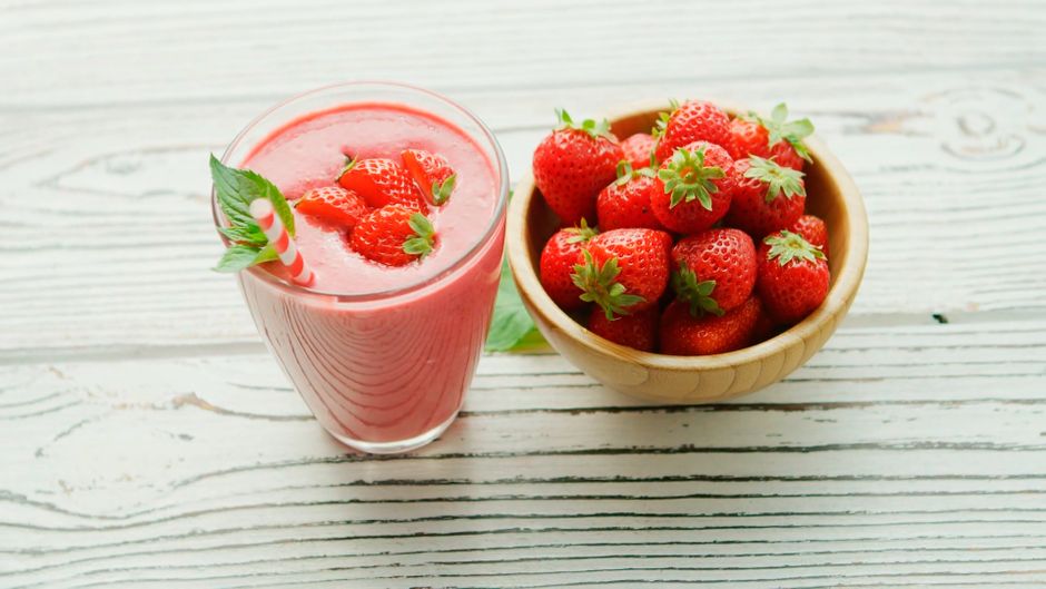 Refreshing strawberry smoothie with a bowl of fresh strawberries on a wooden table.