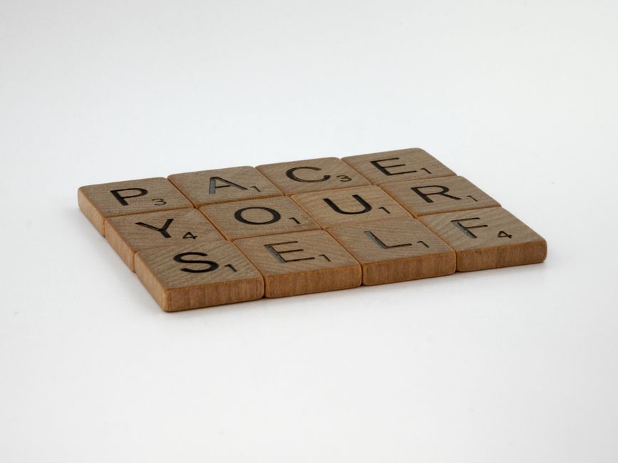 Scrabble tiles form 'Pace Yourself' on a white background, offering a motivational message.
