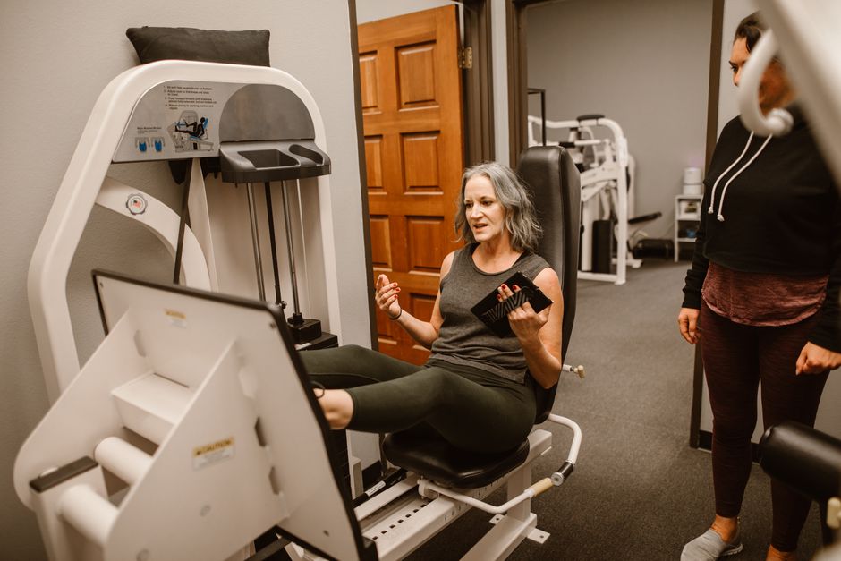 Senior woman working out on a leg press machine with a trainer at a gym.