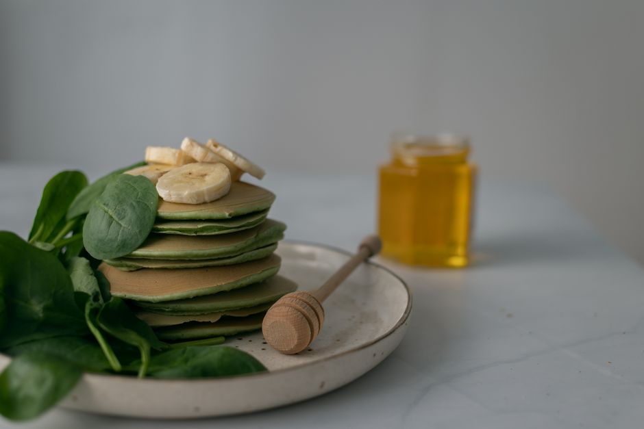 Stack of spinach pancakes with banana slices and honey, perfect for a nutritious breakfast.