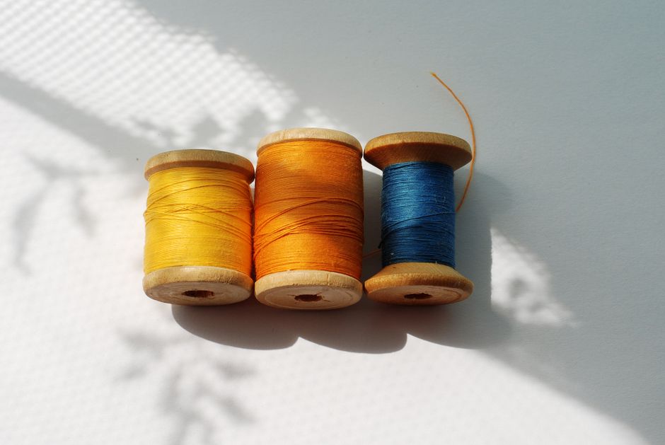Three colorful spools of thread casting shadows on a sunlit surface, portraying a minimalist still life.