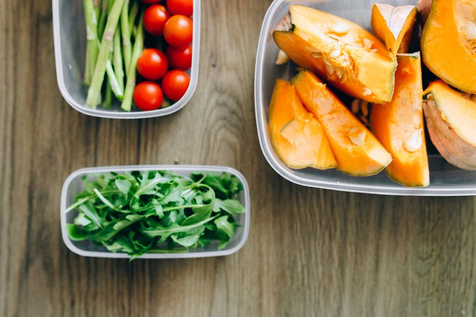 Top view of fresh ingredients including arugula, cherry tomatoes, and squash in plastic containers on wooden background.