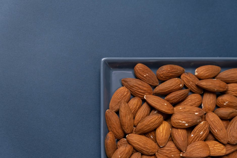Top view of organic almonds in a ceramic dish with a blue background.