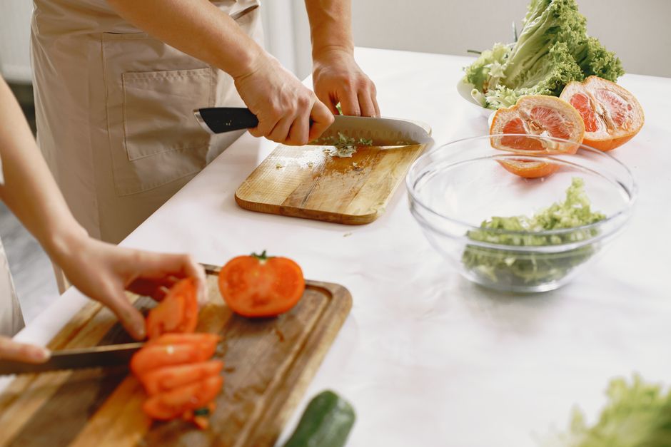 Two people chopping fresh vegetables in a bright kitchen setting.
