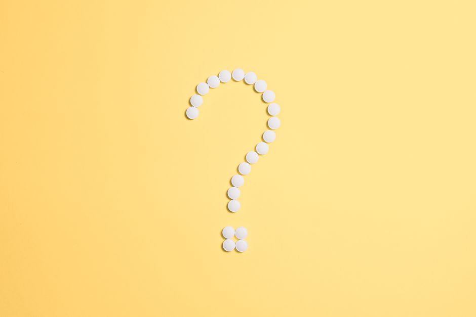 White pills arranged into a question mark shape on a vibrant yellow background.
