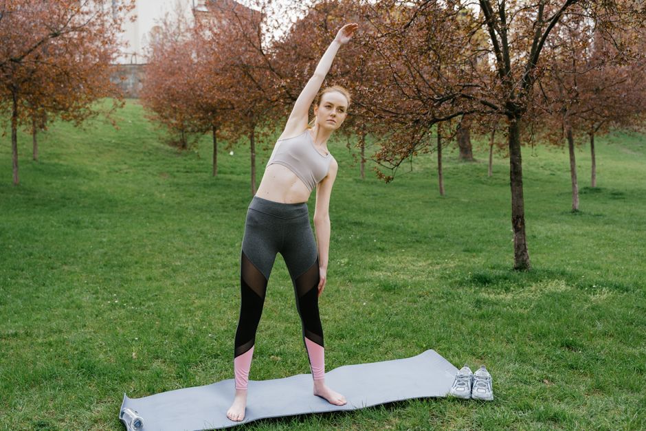 Woman in activewear performing side stretch on yoga mat in a park setting