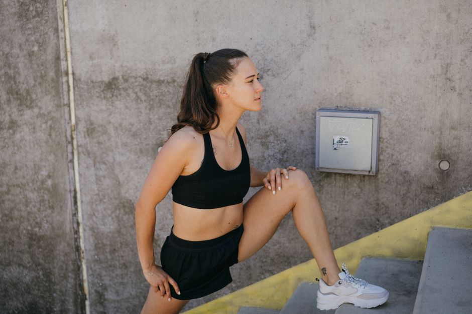 Woman in athletic wear stretching outdoors on steps, embodying wellness and fitness.