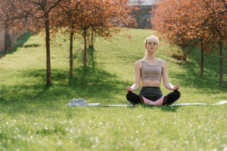 Woman practicing meditation in a sunny park, enhancing wellness and mindfulness.