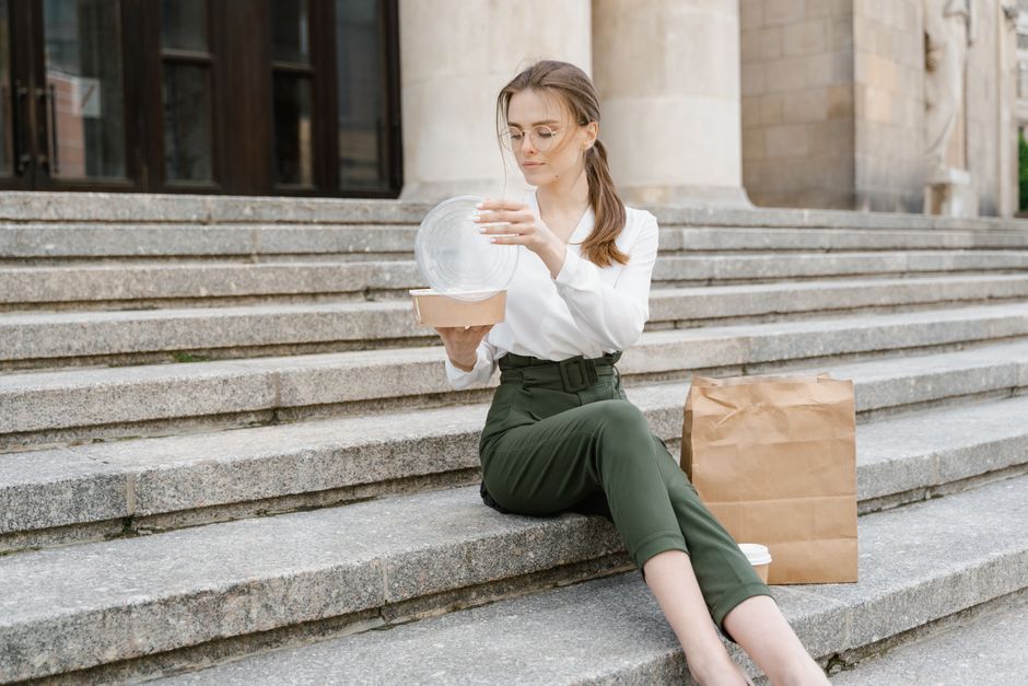 Woman sitting on steps with takeaway meal and paper bag, enjoying a break.