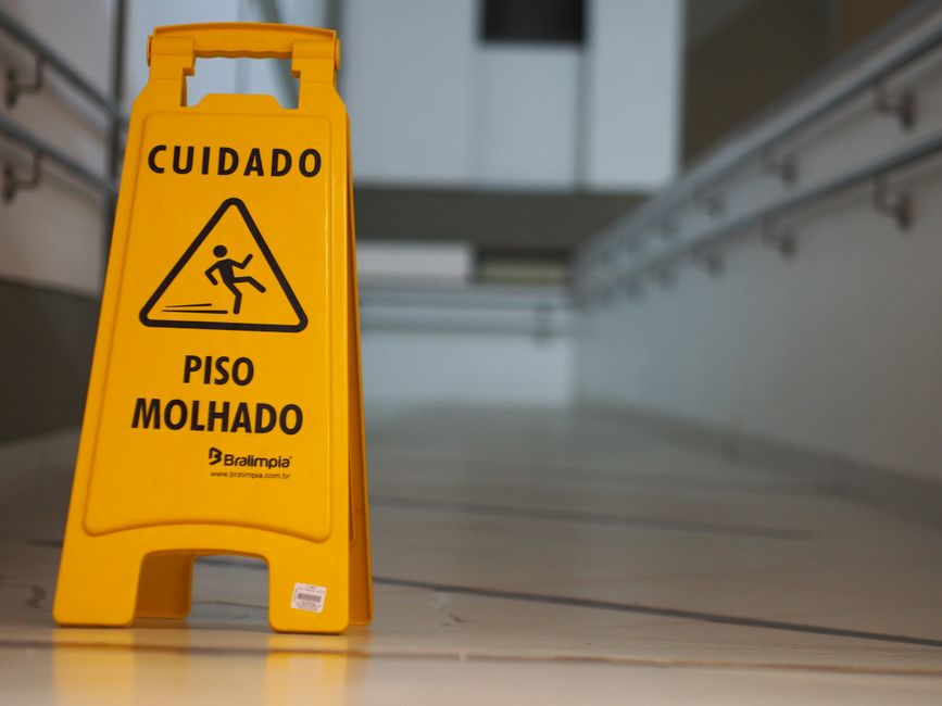 Yellow caution wet floor sign with Portuguese text in an indoor hallway.