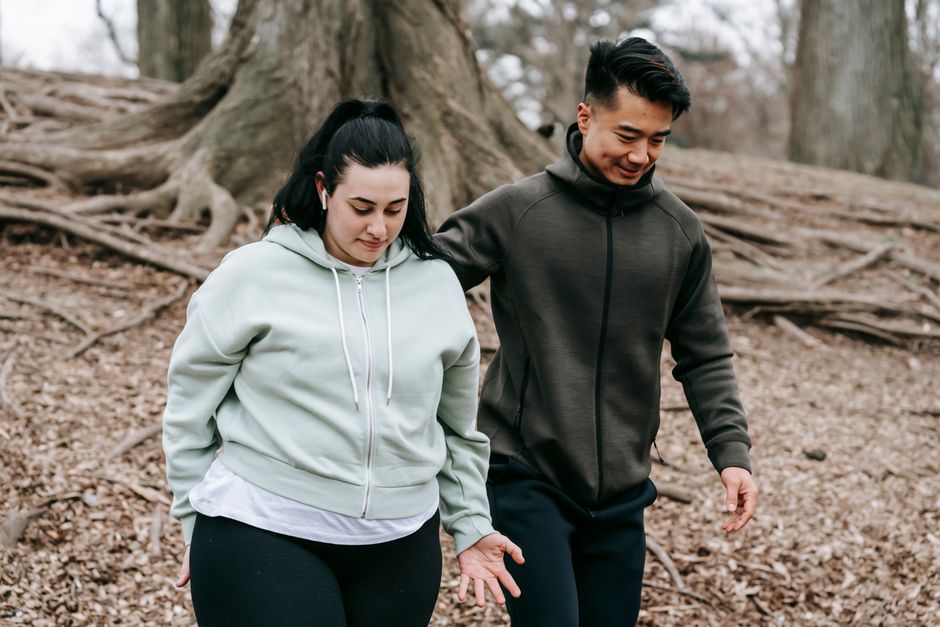 Young diverse overweight female and instructor strolling in park with majestic trees in daytime