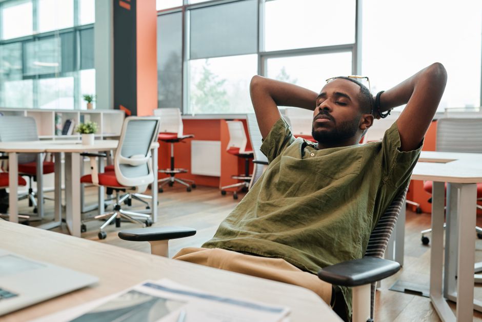 Young man resting in an office chair, eyes closed, in a modern workspace. Captured with a DSLR camera.