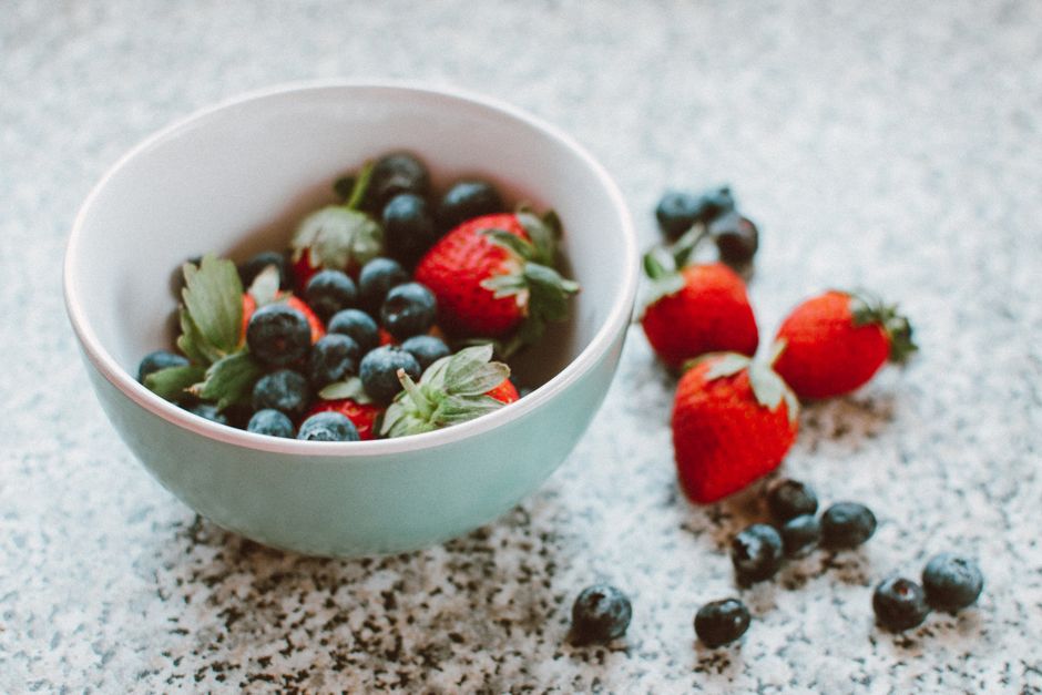 A blue bowl filled with fresh strawberries and blueberries on a speckled surface.