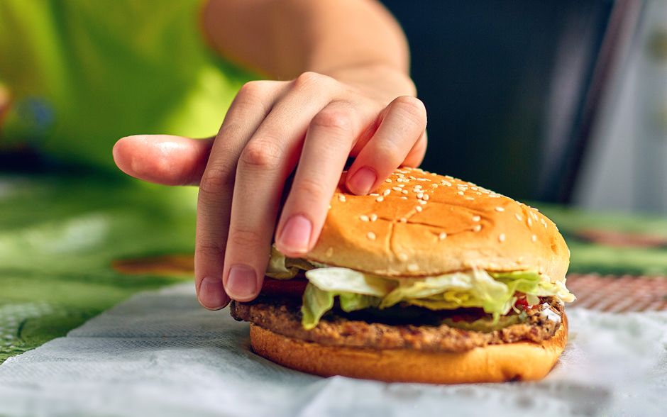 A close-up of a person's hand reaching for a juicy burger with lettuce, depicting a delicious fast-food moment.