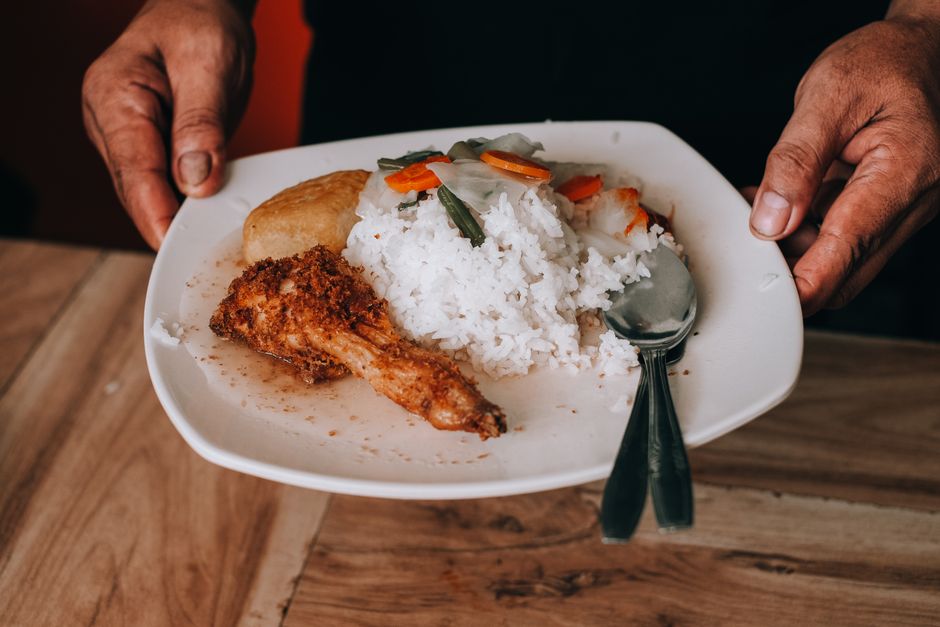 A close-up of a plate with rice, fried chicken, and vegetables served with a spoon.
