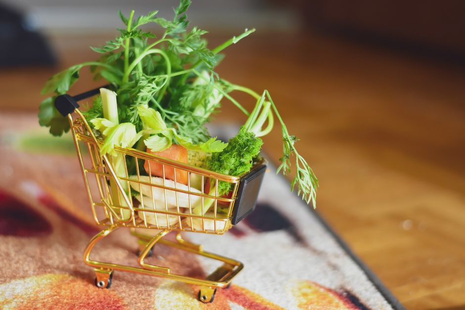 A close-up of a tiny shopping cart filled with fresh vegetables on a patterned surface.