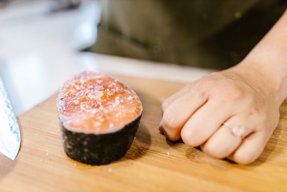 A close-up view of a fresh salmon fillet next to a hand on a cutting board.
