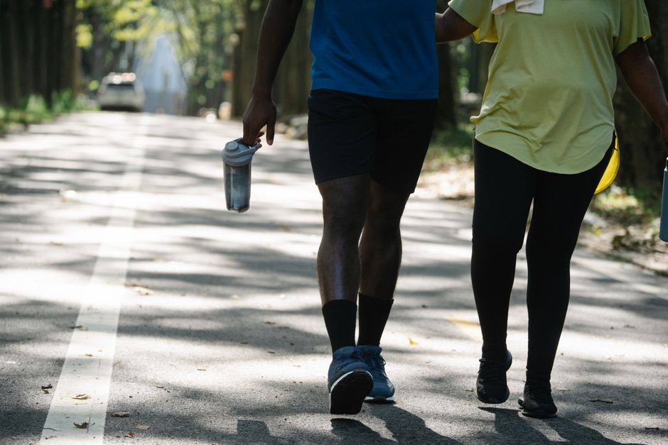 A couple enjoying a walk outdoors, holding tumblers on a sunny day.