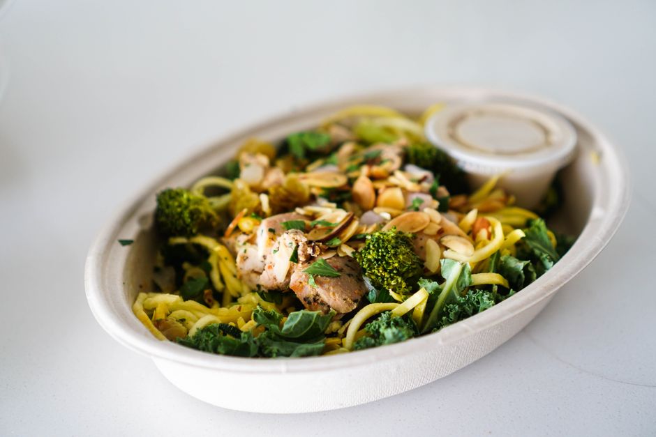 A delicious bowl of grilled chicken, broccoli, and zucchini noodles topped with almonds.