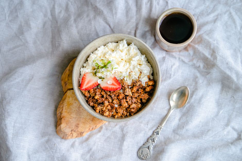 A delicious breakfast bowl with cottage cheese, granola, and strawberries served with black coffee.