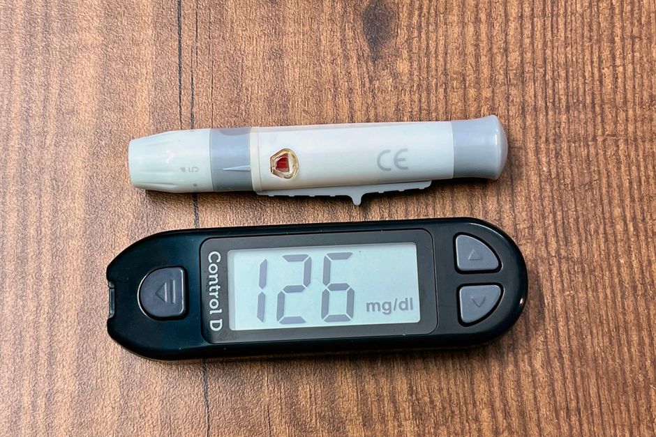 A digital glucometer displaying 126 mg/dL with a lancing device placed on a wooden surface.