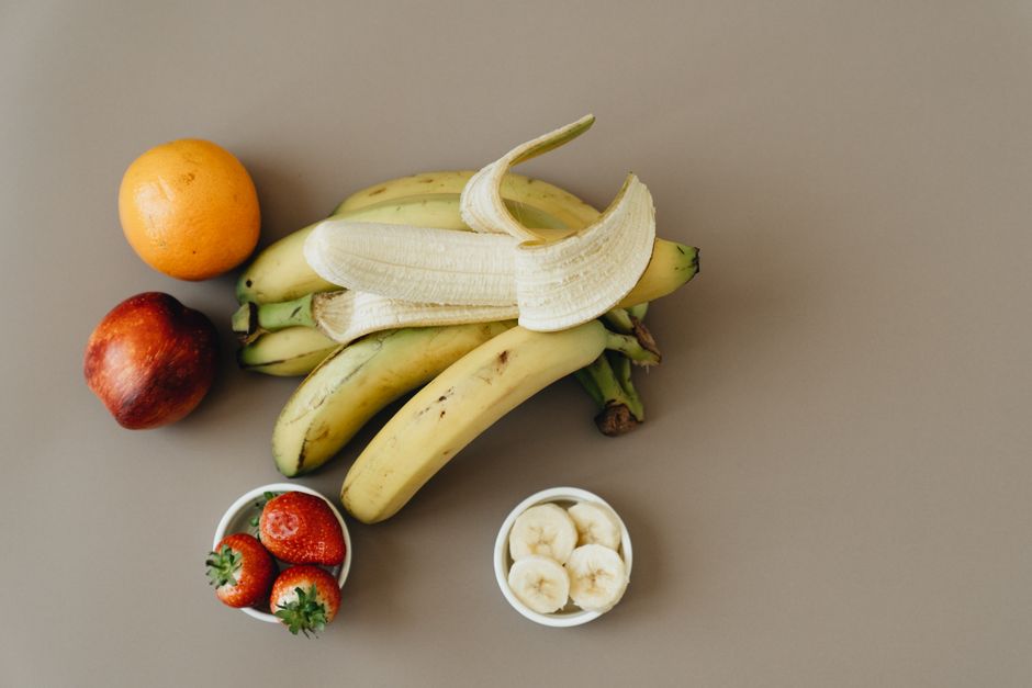 A diverse collection of fresh fruits including bananas, orange, apple, and strawberries.