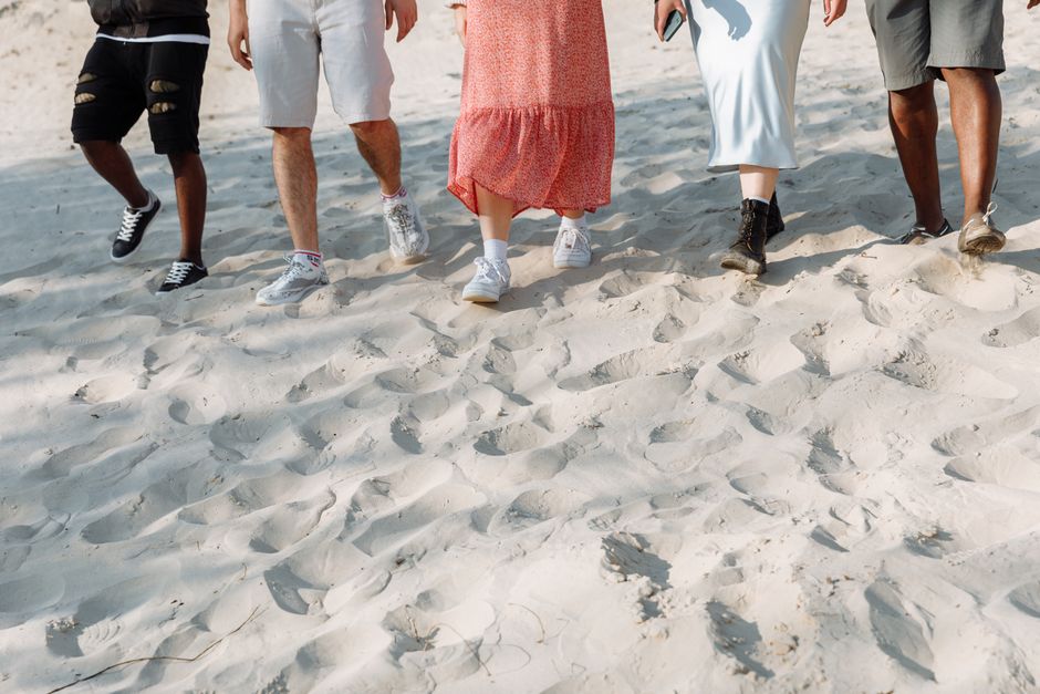 A diverse group of people walking on a sandy beach, showcasing summer fashion and casual footwear.