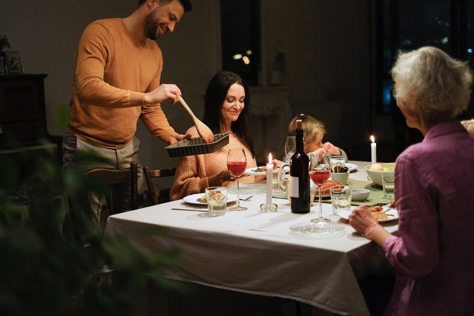 A family enjoys a warm dinner together around a candlelit table with wine and laughter.