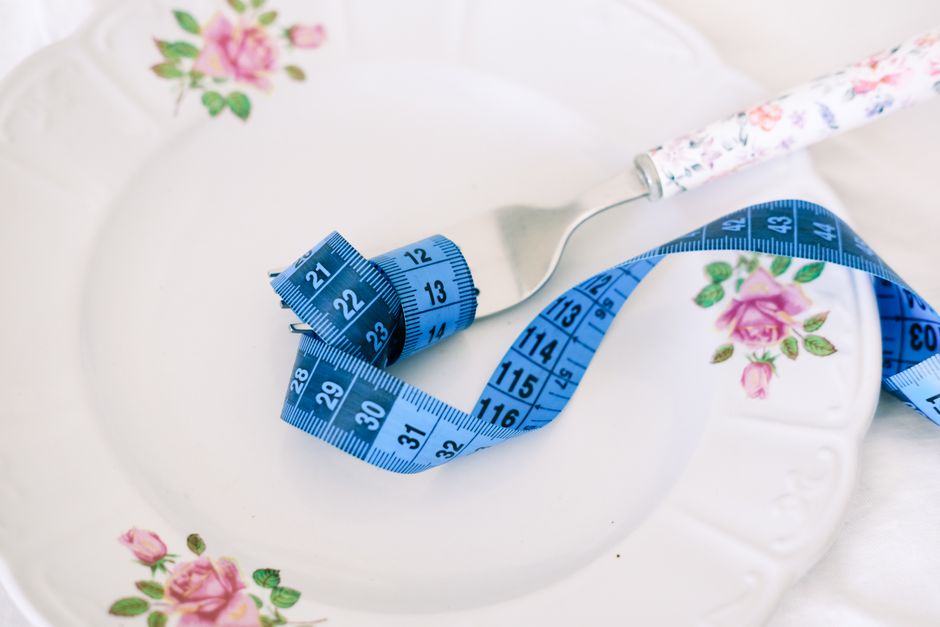 A floral plate with a fork and blue measuring tape symbolizing dieting or healthy eating.
