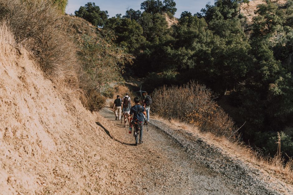 A group of people hiking on a scenic outdoor dirt trail surrounded by greenery and hills.