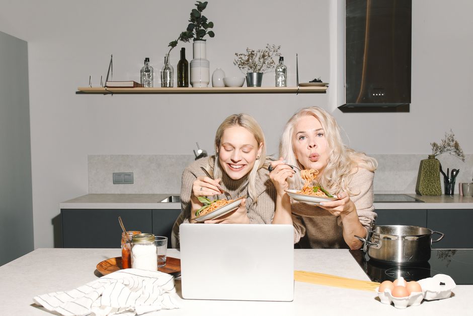 A joyful mother and daughter duo savoring pasta in a modern kitchen, sharing family time.