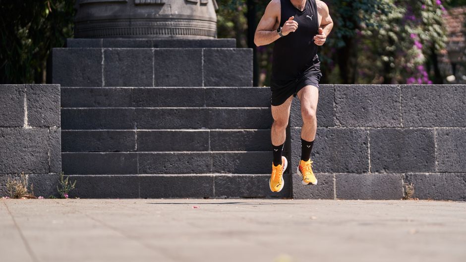 A male athlete jogging on stone steps wearing a black outfit and orange shoes.