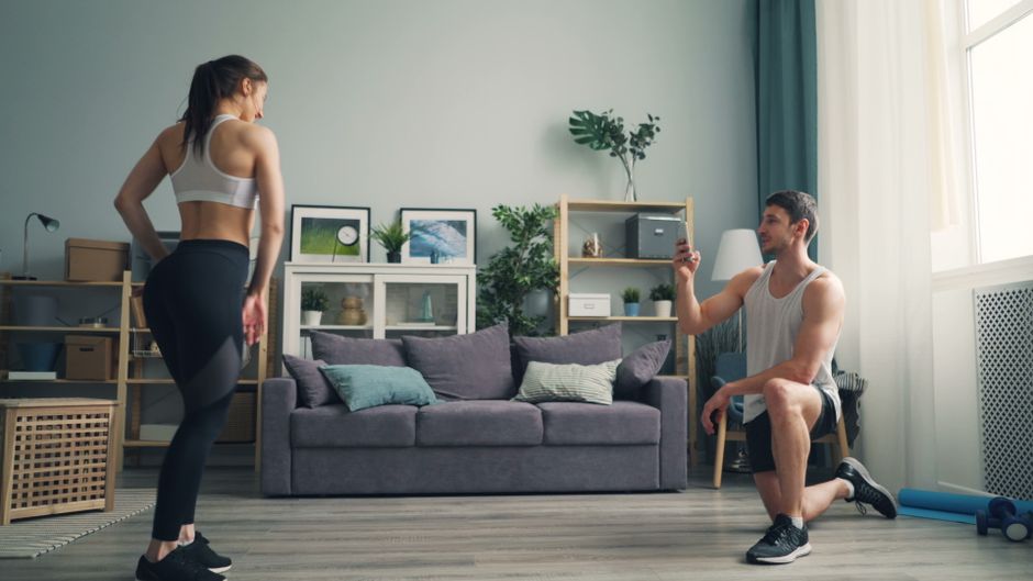 A man and woman in sportswear exercising together in their living room.