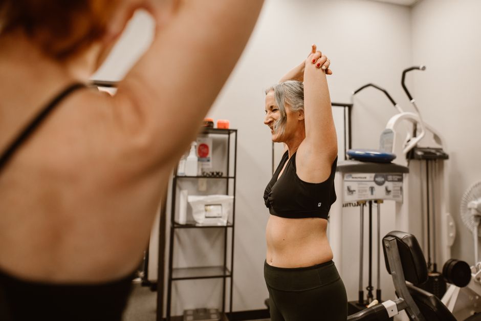 A middle-aged woman confidently stretches in a gym, embracing wellness and healthy living.