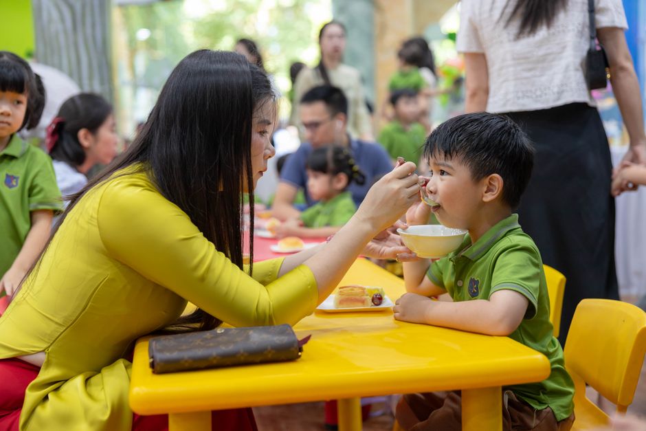 A mother lovingly feeds her child at a colorful kindergarten setting, capturing a moment of care and connection.