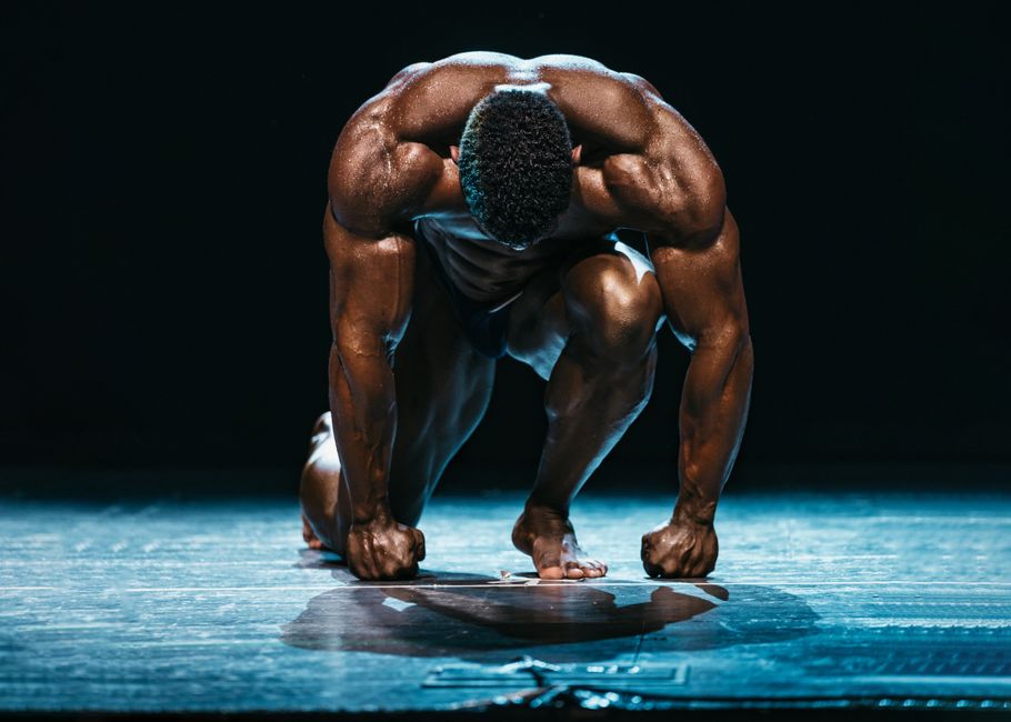 A muscled athlete prepares to start a race on stage under dramatic lighting.