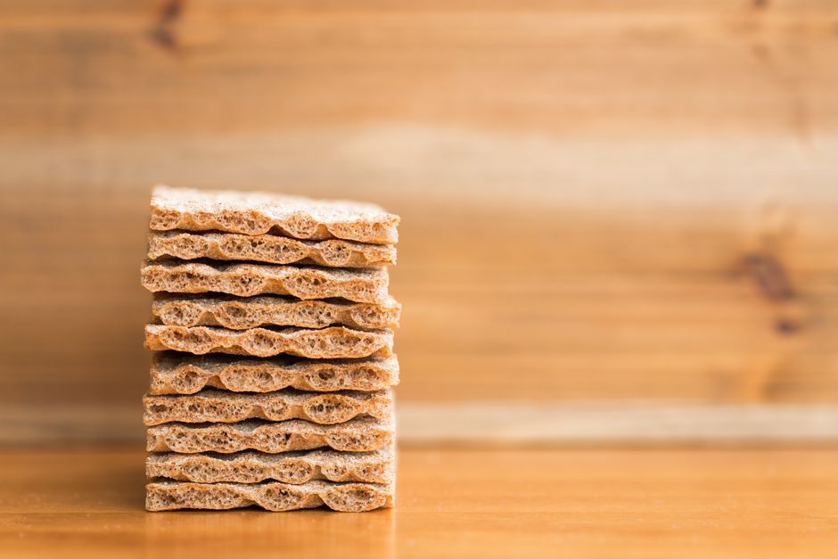 A neatly stacked pile of crispbread sits on a wooden surface with a blurred wooden backdrop.