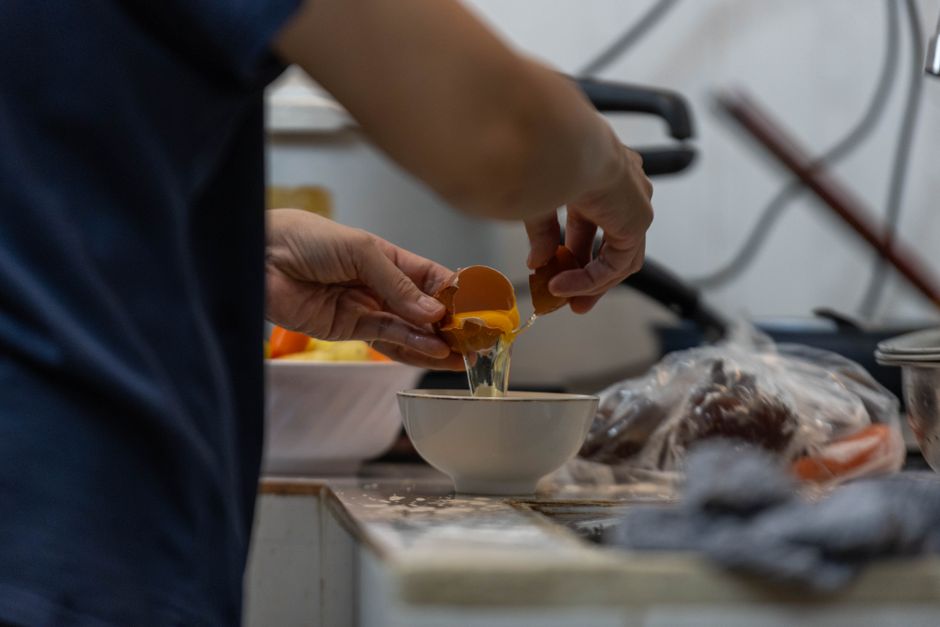 A person cracks an egg into a bowl, capturing the process of cooking preparation.