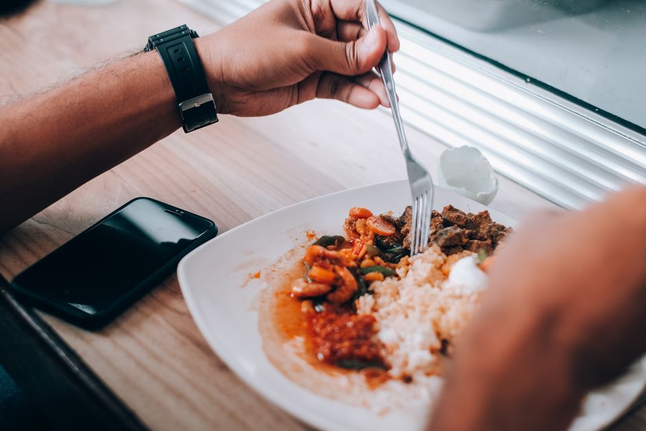 A person enjoys a meal of rice with mixed vegetables by a window.