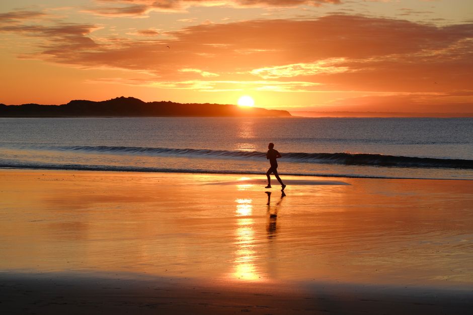 A person running on a beach at sunrise in Australia, reflecting tranquil fitness and nature.